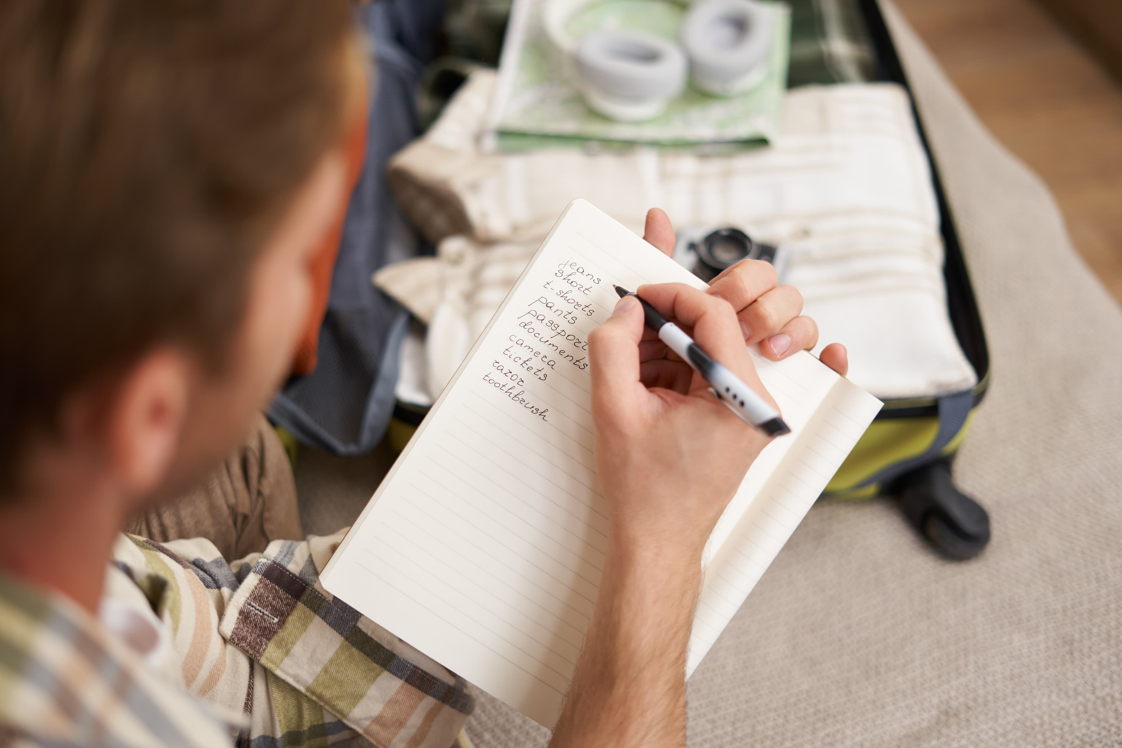Writing a travel packing list beside an open suitcase